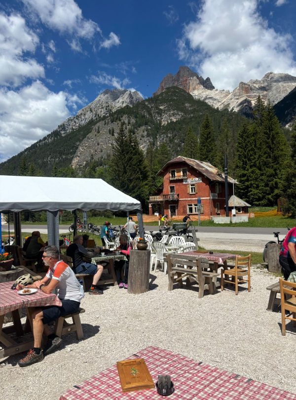 Alta Via 1 hikers relax at an outdoor cafe with Dolomites mountains in the background.